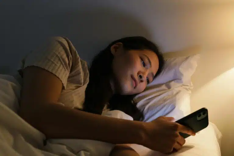 femme qui regarde son t&eacute;l&eacute;phone au lit mauvaises habitudes sommeil repos bien dormir &eacute;crans le soir
